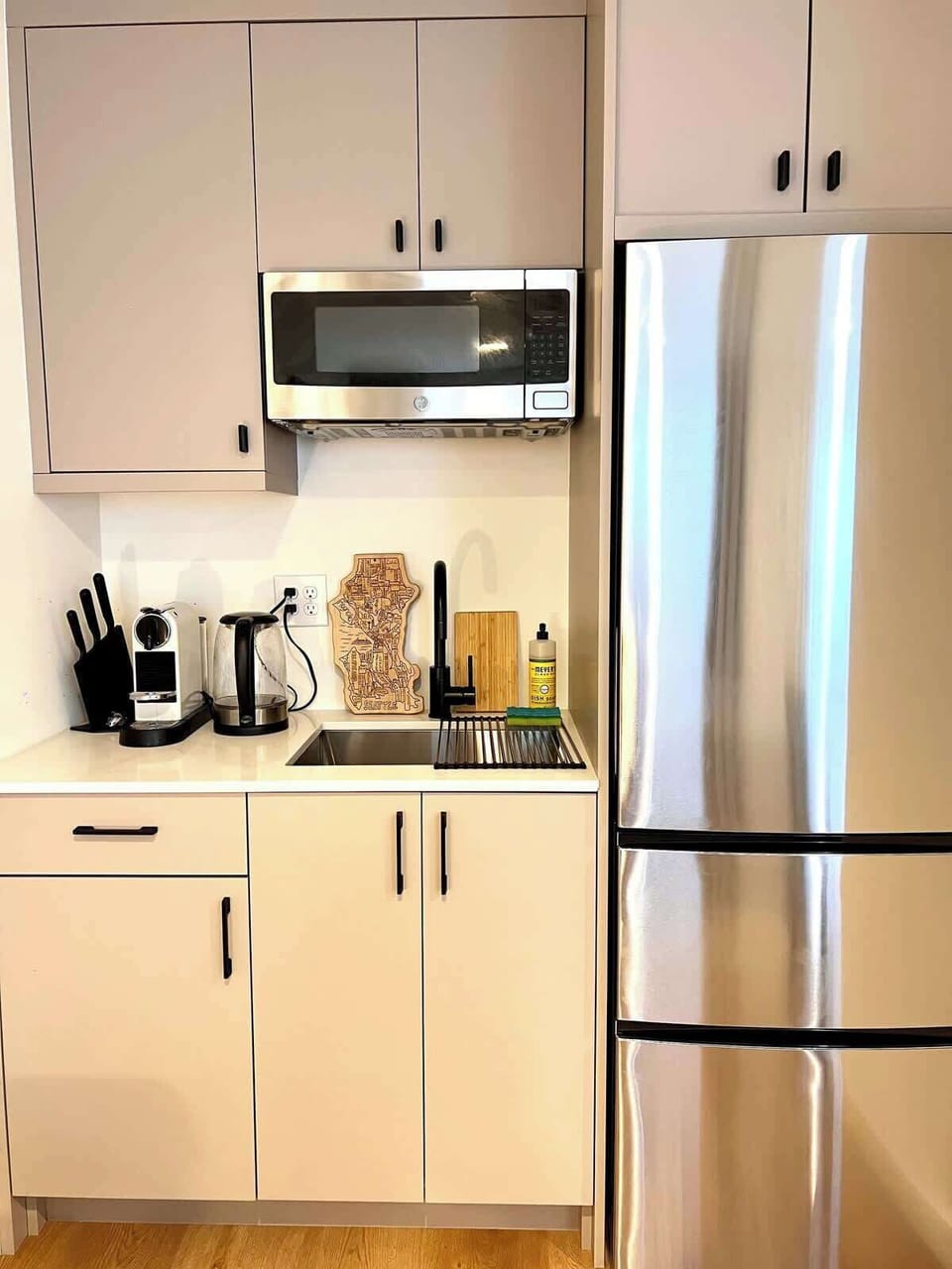 Bright modern kitchen with sleek cabinetry, stainless steel fridge, built-in microwave, and a clean, functional design.