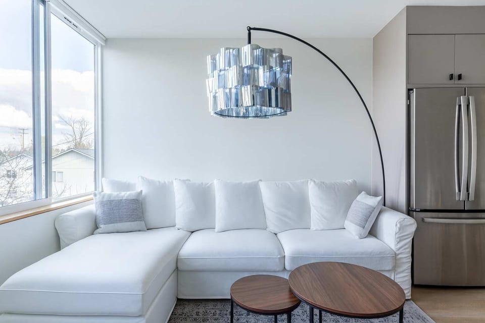 Stylish open living space featuring a cozy sectional sofa, statement lighting, natural light, and a clean, contemporary design.