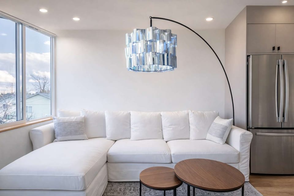 Sunlit living area with plush sectional sofa, elegant arc lamp, modern chandelier, and large windows offering peaceful mountain views.