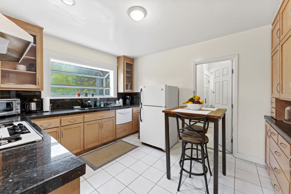Sunlit kitchen: fridge, table, chairs, clock.