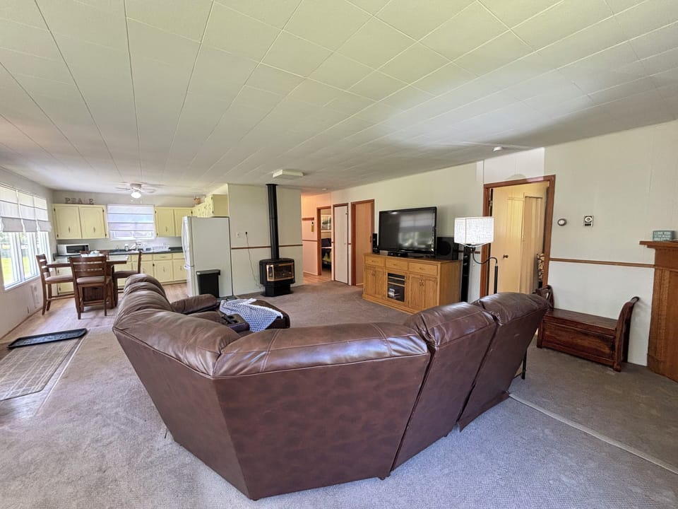 A spacious, open-concept living area with a brown leather sectional sofa facing a wooden entertainment center with a flat-screen TV.