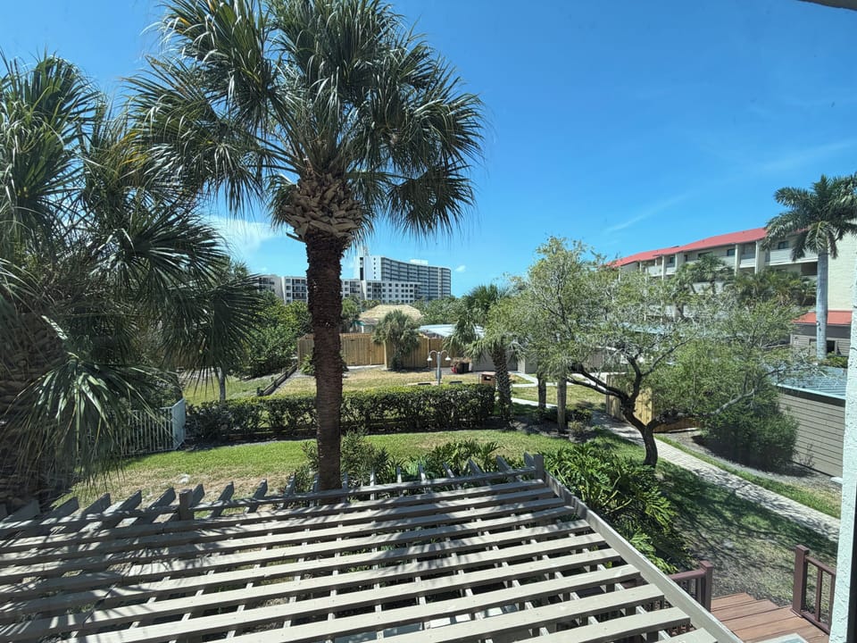 The property sits in a lush tropical neighborhood with palm trees and mature landscaping, surrounded by nearby residential buildings and high-rises visible in the background.