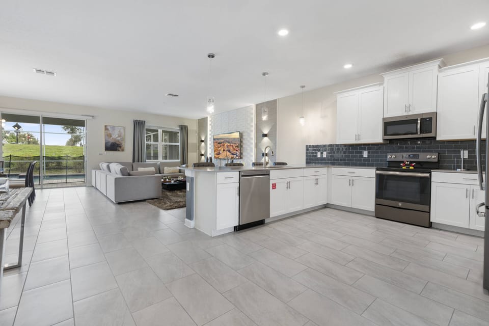 Enjoy cooking in this bright, spacious kitchen with sleek white cabinetry and modern stainless steel appliances. Large windows bring in natural light, creating a warm, inviting atmosphere for all your culinary adventures.