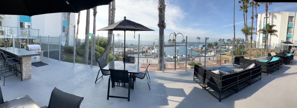 Upper deck of pool area overlooking harbor and pier with tables and BBQ's