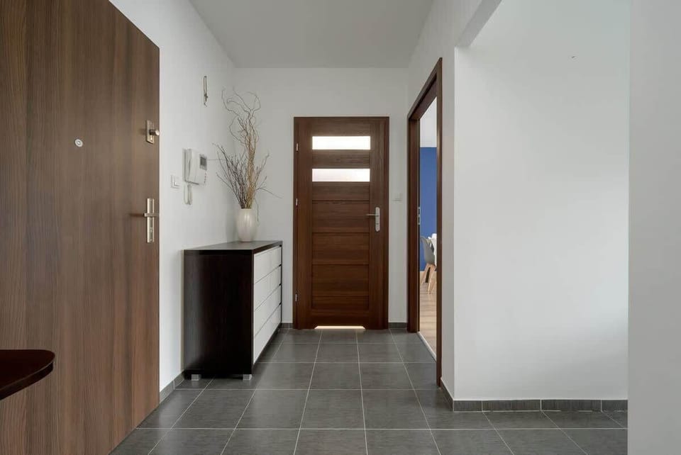 A bright and modern entrance hallway featuring a sleek wooden door, tiled flooring, and a minimalist console table for convenience.

