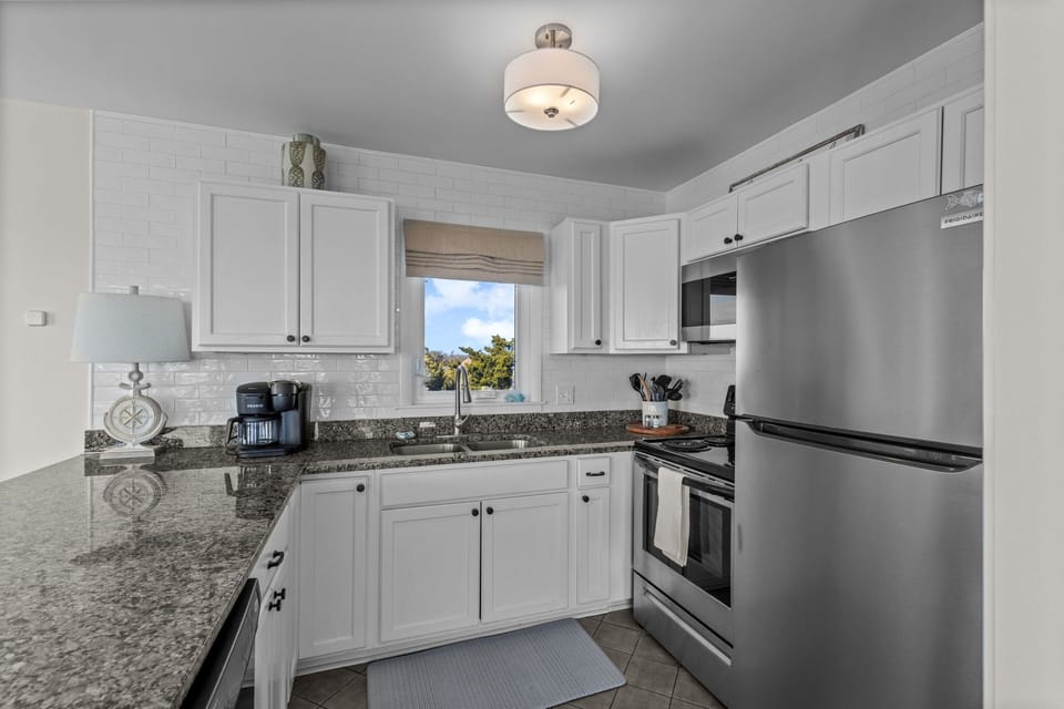 Cook your favorite meals in this bright, fully-equipped kitchen featuring granite countertops, white cabinetry, and modern stainless steel appliances.