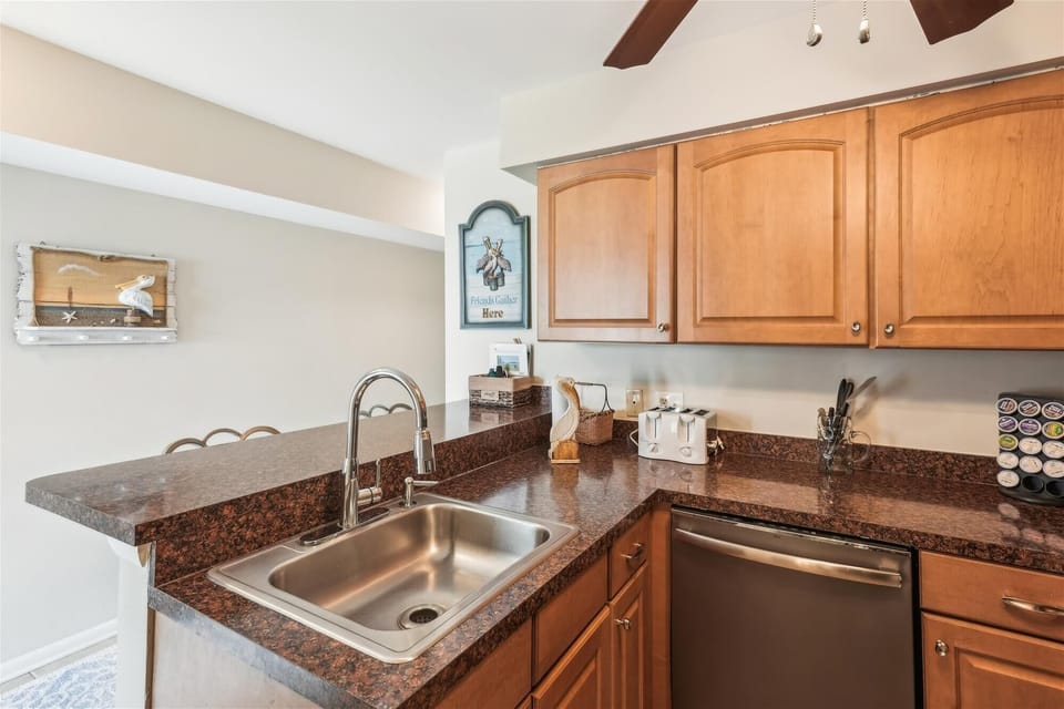 Your fully-equipped kitchen awaits with warm wood cabinetry, granite countertops, and thoughtful touches like coastal decor and a well-stocked coffee station—perfect for preparing meals at your leisure.