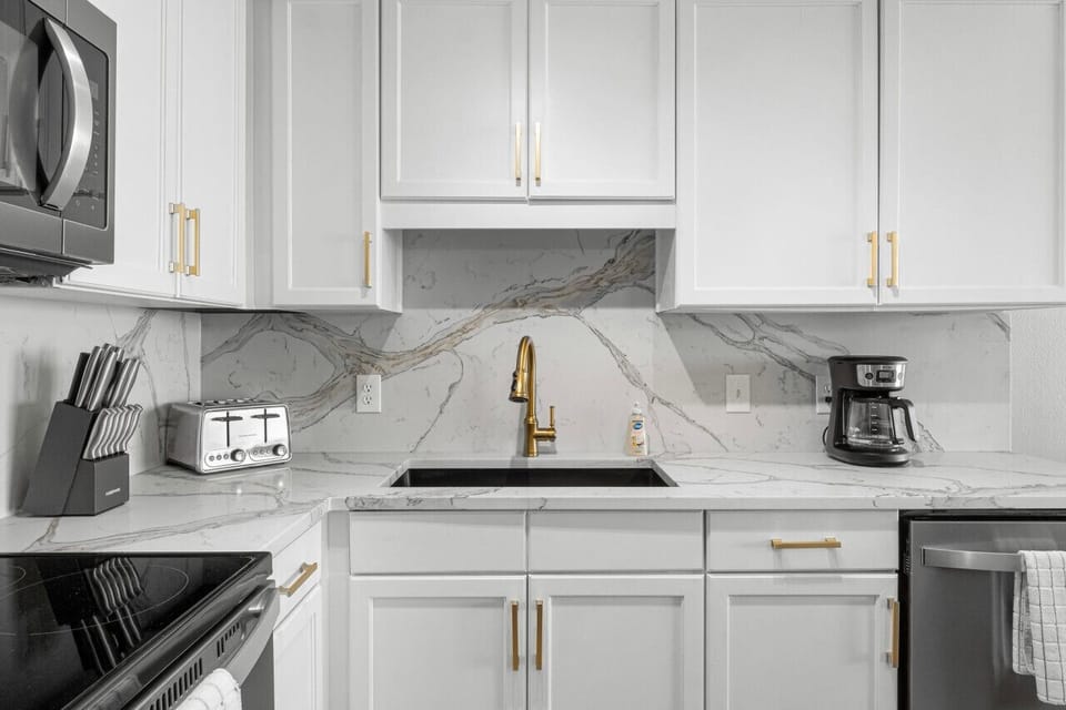 Fully equipped modern kitchen with sleek appliances, marble-style backsplash, and elegant gold accents for a touch of luxury