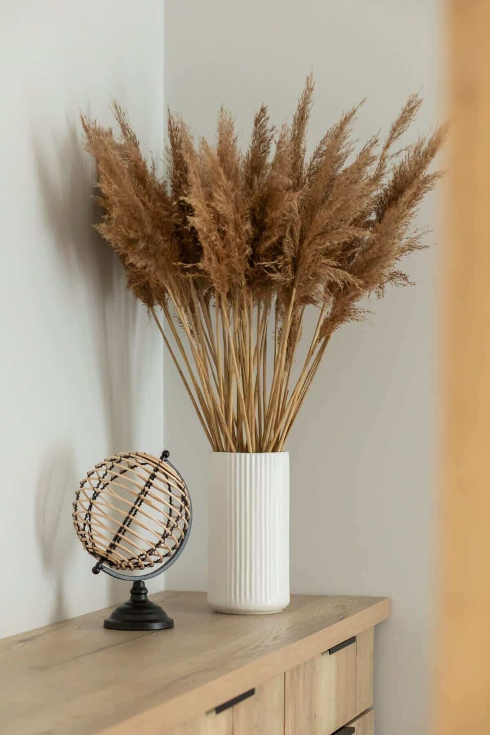 A decorative corner featuring a wooden side table, a dried wheat arrangement, and a small modern clock for an elegant touch.

