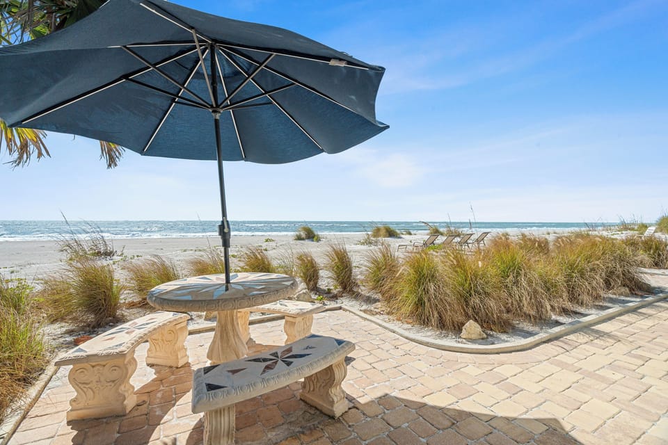 Beachfront seating area with umbrella shade and ocean views, featuring natural dune landscaping.