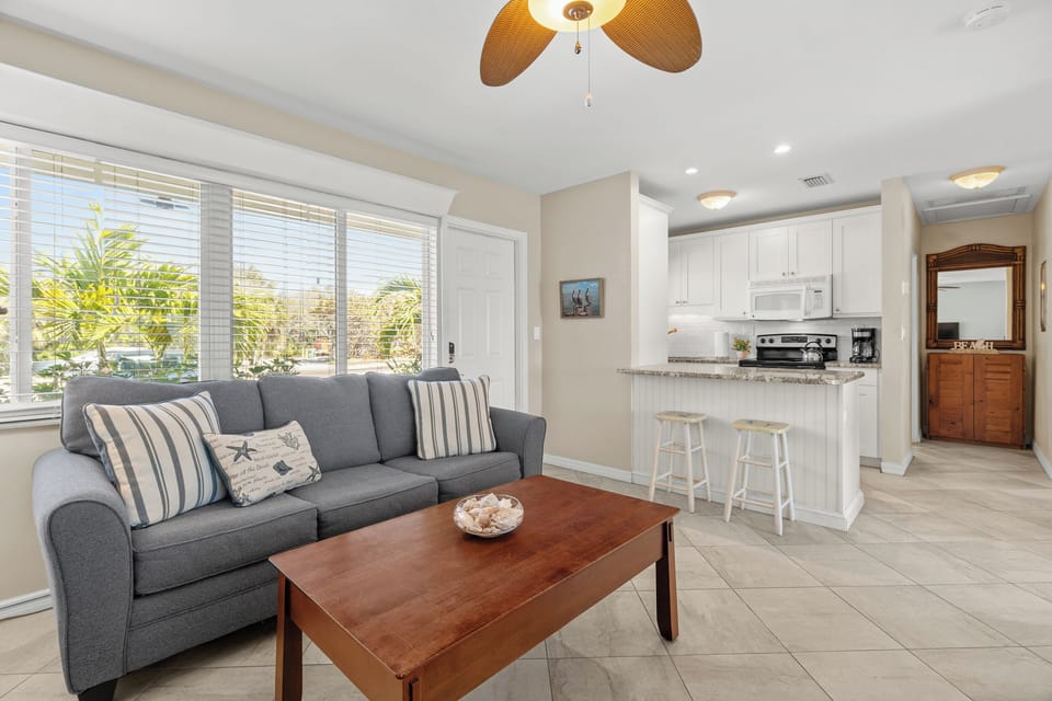 Relax in your bright, coastal-themed living space where comfortable seating flows into a fully equipped kitchen perfect for preparing meals together.
