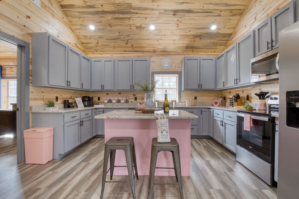 Fully equipped kitchen with a pink island, coffee bar, and warm cabin-style woodwork.