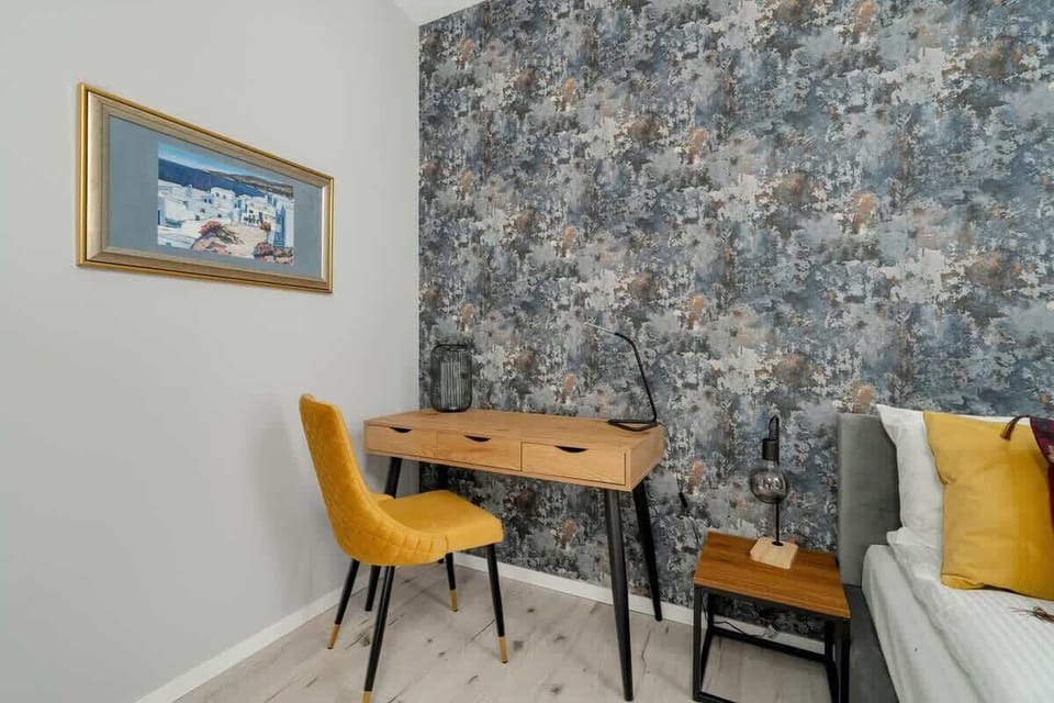 A cozy bedroom corner with a comfortable bed, a wooden bedside table, and an accent wall with patterned wallpaper.







