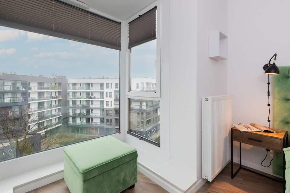A bright corner of the bedroom with a seating area, a large window, and a view of the surrounding cityscape.

