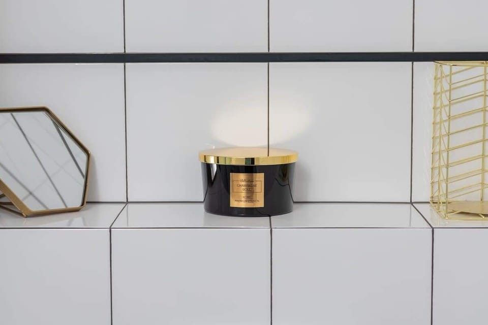 A close-up of a decorative bathroom shelf with a golden mirror and a black-and-gold candle, enhancing the modern aesthetic.

