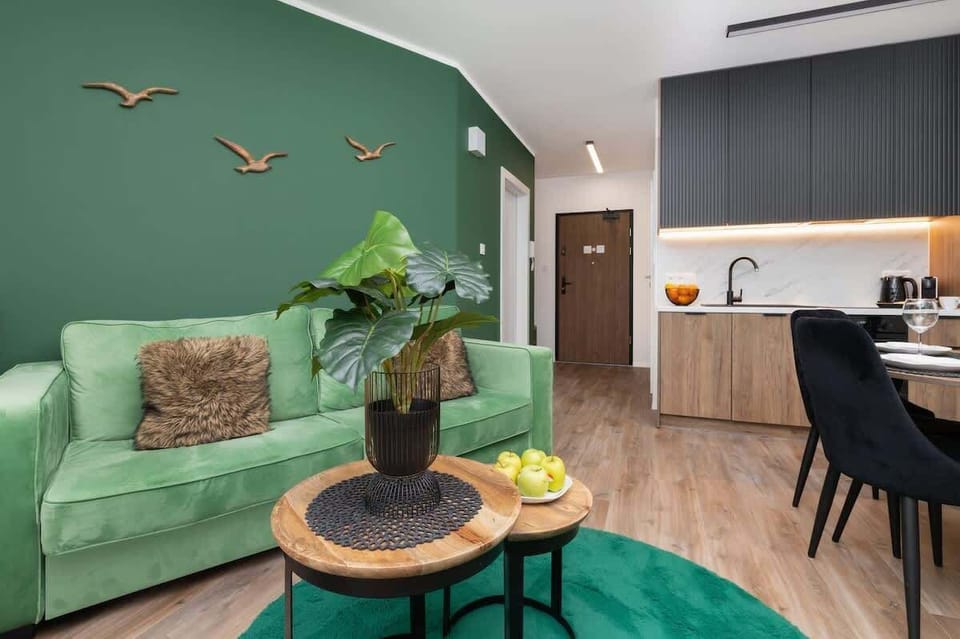 Another angle of the living area, showcasing the green sofa, decorative pillows, and an open-plan layout connecting to the kitchen.

