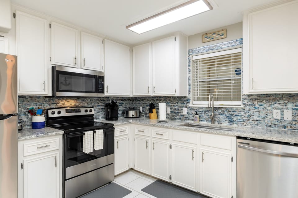 Your fully equipped kitchen awaits with granite counters, stainless appliances, and coastal-inspired tile backsplash—perfect for preparing meals.