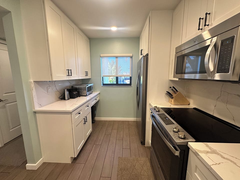 Your fully equipped galley kitchen features pristine white cabinets, marble countertops, and stainless steel appliances for effortless meal preparation.