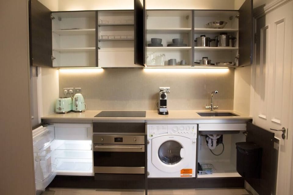 Open Kitchen with oven-microwave, stove, mini-fridge, washing machine/dryer, coffee machine, kettle, toaster, and kitchenware.