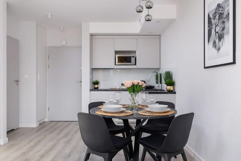 A well-lit dining area with a round black table, four chairs, and a simple, elegant centerpiece adding charm to the space.

