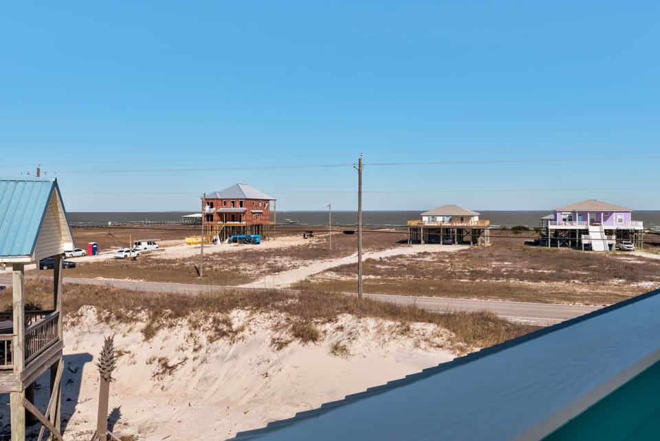 Coastal community with elevated beach houses scattered across sandy dunes under clear blue skies.