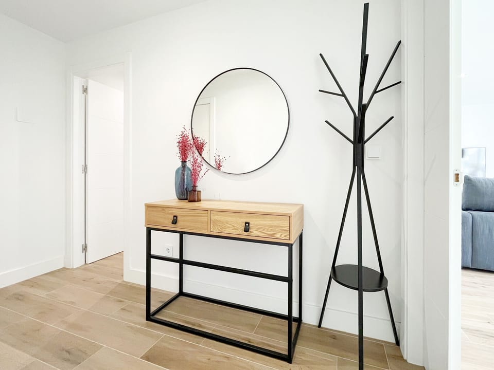 Elegant entryway or reception area featuring an industrial-style wood and metal console table, a modern round mirror, and a designer coat rack. The minimalist and functional decor provides a bright welcome to the apartment.