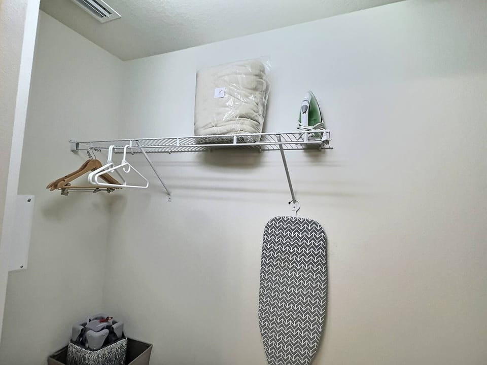 This functional space includes a sleek metal rack for neatly stored linens and hangers, offering an ideal spot to organize your belongings. With an iron and patterned ironing board, you'll look your best throughout your stay.