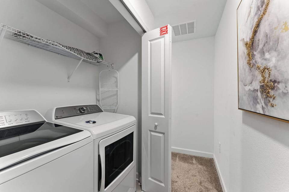 Step into a well-equipped laundry nook featuring sleek, modern appliances complemented by clean, white cabinetry. The subtle artwork adds a touch of style, ensuring your laundry experience is both practical and pleasant.