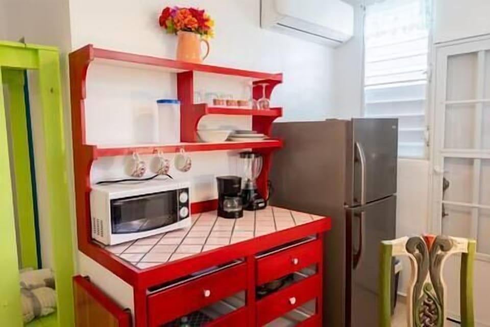 Kitchen area with essentials: microwave, refrigerator, coffee maker, blender, electric pan. 