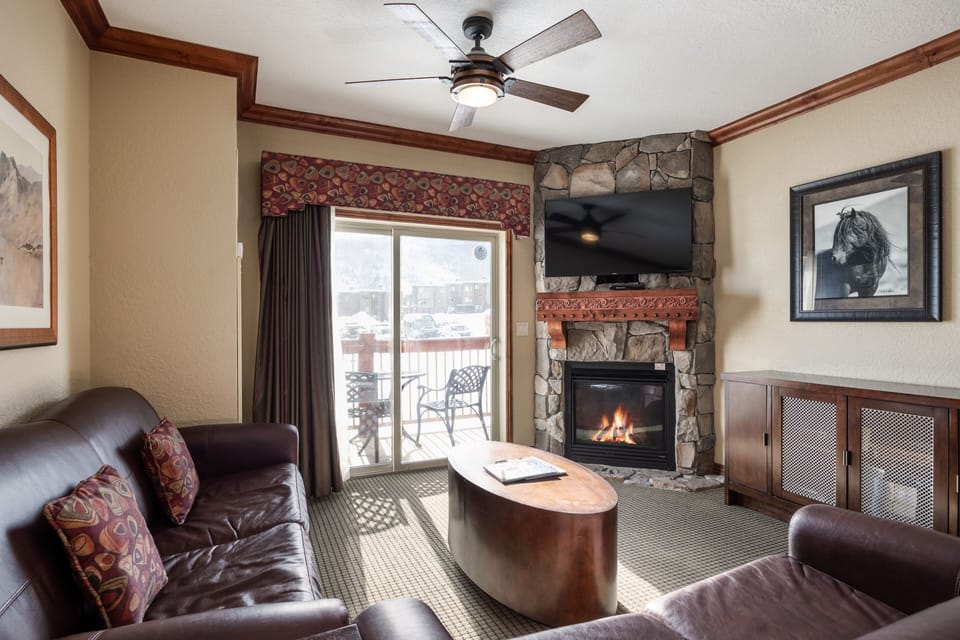 - Gather in the living room featuring a stone fireplace and smart TV  
- Comfortable leather seating with direct access to the private balcony  
- Warm up after skiing while enjoying mountain views from indoors