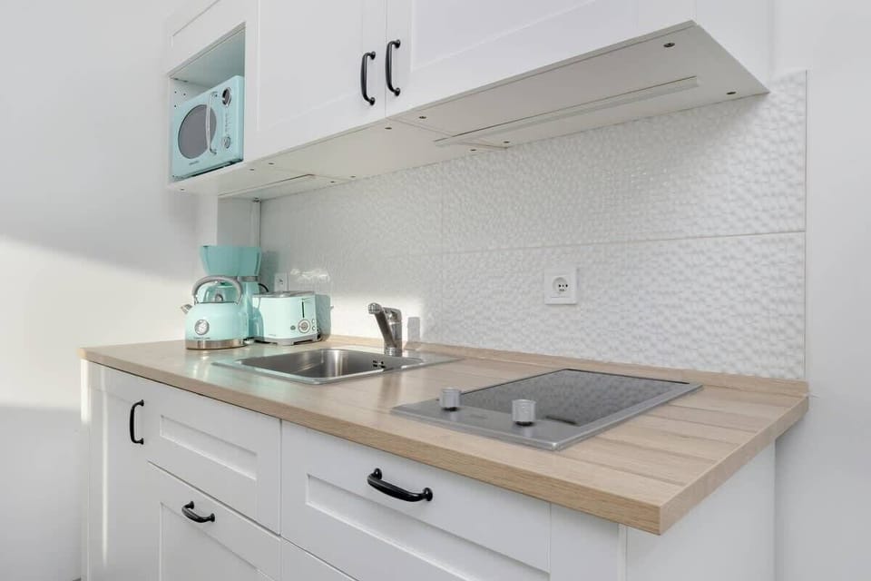A compact yet fully equipped kitchen with sleek white cabinetry, a modern countertop, and pastel-colored kitchen appliances that enhance its stylish design.