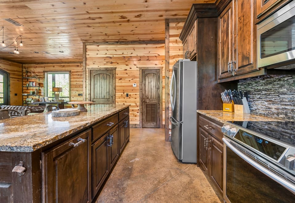 The kitchen shows off its warm, wooden design featuring a  sleek appliances, with a glimpse into the adjacent rooms.