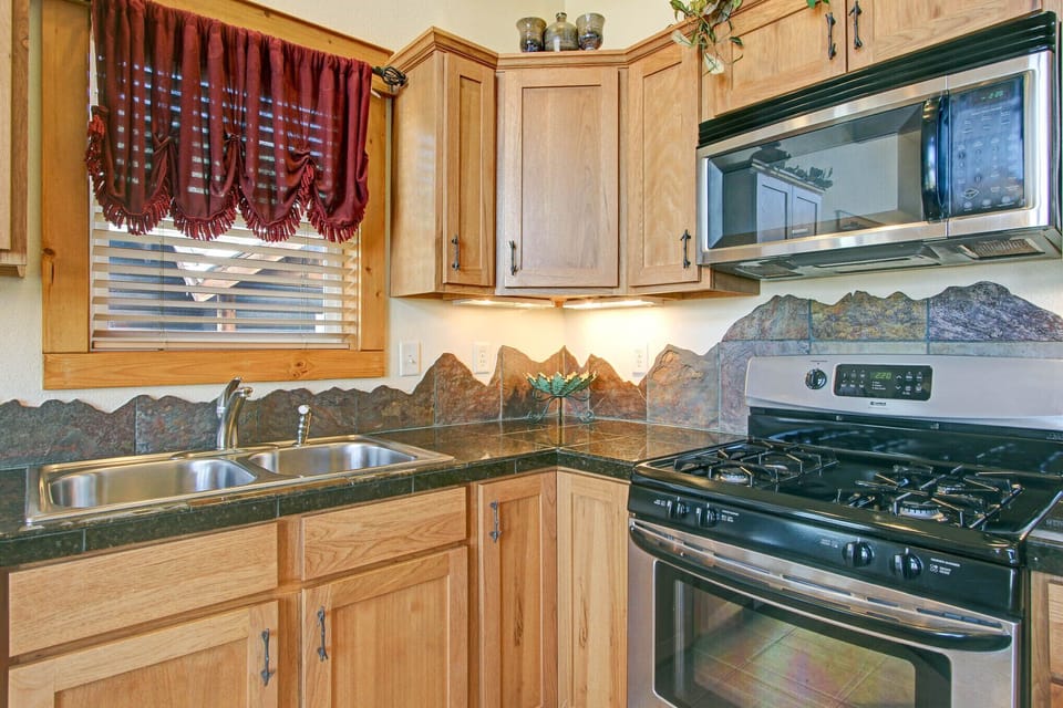 Beautifully decorated full kitchen. Mountain-themed granite backsplash along countertops. Full size refrigerator, dishwasher, gas stove/oven and microwave.