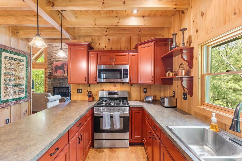 - Bright kitchen with gas stove and stainless steel oven for cooking   - Open counter design with views of the living room and fireplace   - Perfect for preparing home-style meals during your cabin stay