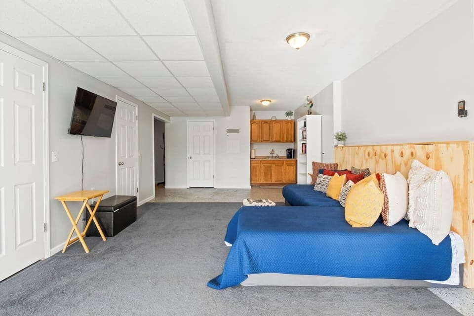 Maximize your relaxation in this versatile basement living space, equipped with comfortable bedding, a cozy TV area, and a kitchenette for convenience.