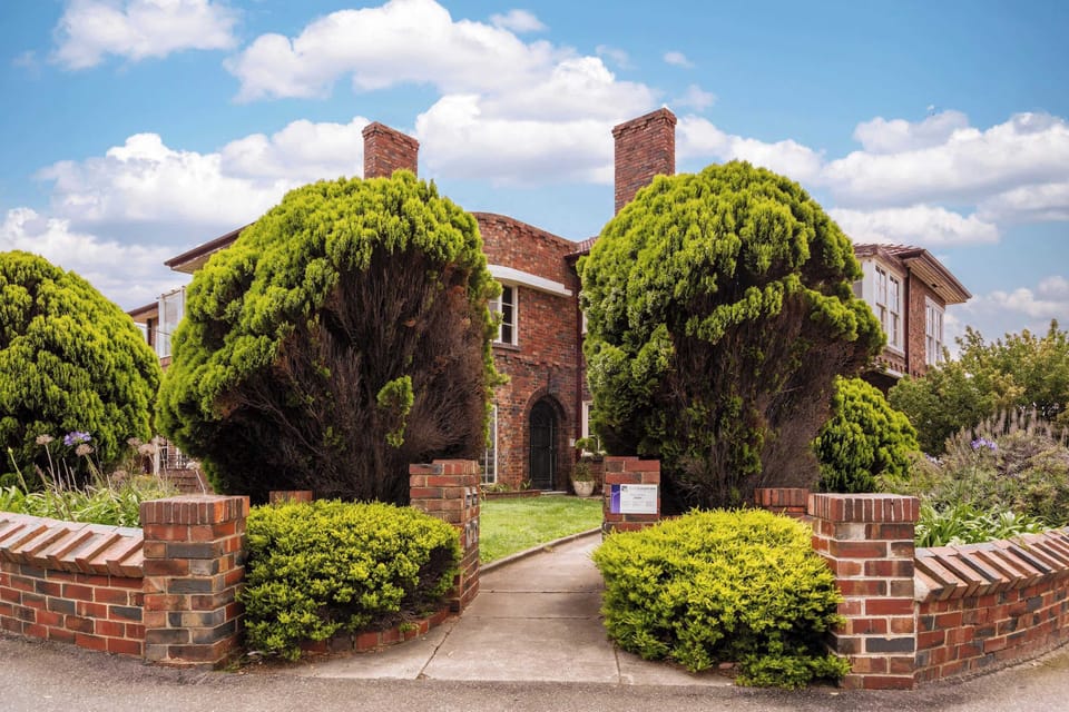 EXTERIOR: A charming brick archway leads to the front door, framed by lush greenery