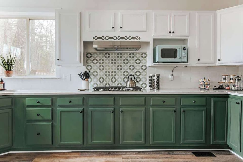 Kitchen features green cabinets and patterned tile backsplash.