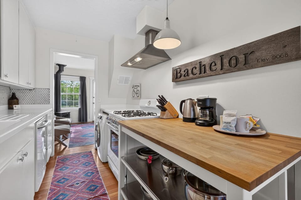 Butcher block counter holds coffee maker, kettle, and knife set above open stainless steel shelving.