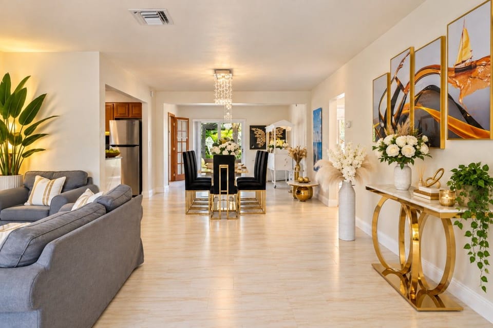 Stunning Open Concept Design! Seamless flow from living to dining with crystal chandelier, gold accents & modern artwork. Bright, spacious layout perfect for gatherings. Complete Hollywood Beach villa with game rooms, hot tub & beach 3min away!