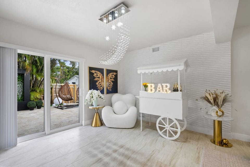 ✨ Elegant Lounge with BAR Cart & Crystal Chandelier! Stunning textured walls, butterfly artwork & unique white chair create Instagram paradise. Opens to tropical patio with hanging chair. Hollywood Beach villa with game rooms, hot tub & beach nearby!