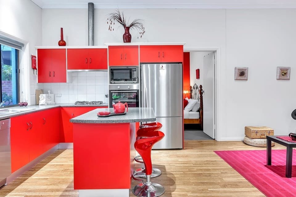 The kitchen features an invigorating splash of vivid red in the cabinetry and island bench. Bar stools provide additional casual dining space at the countertop. 
