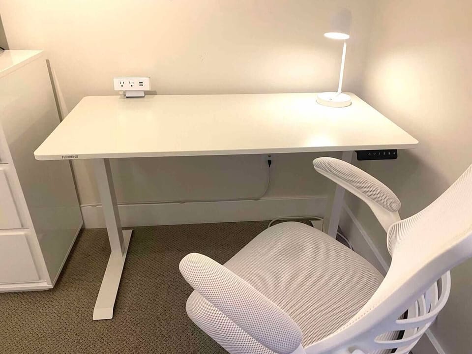Sit-stand desk with task chair, light, and power strip in second bedroom.