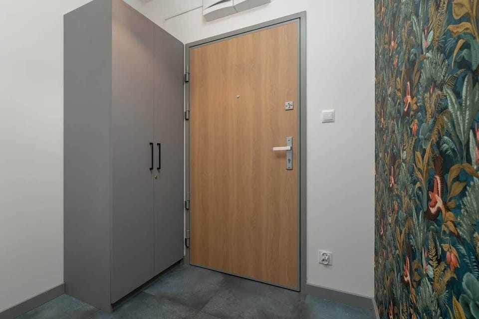 A corridor with patterned wallpaper and wooden doors next to which stands a grey spacious wardrobe. 
