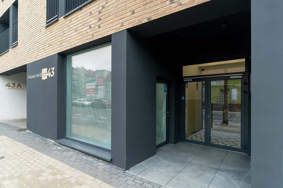The entrance to the apartment building with a glass door and minimalist architecture. The structure is finished in dark tones with modern design elements.