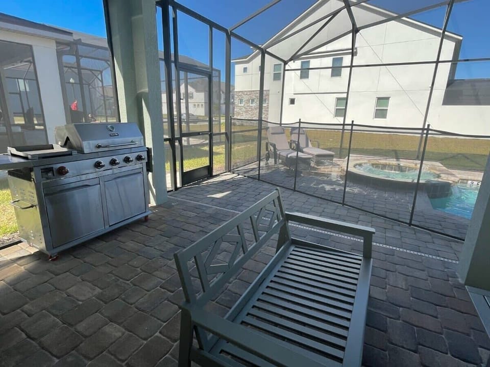 Screened patio with a stainless-steel grill, outdoor seating, private pool, and raised hot tub for sunny group gatherings.