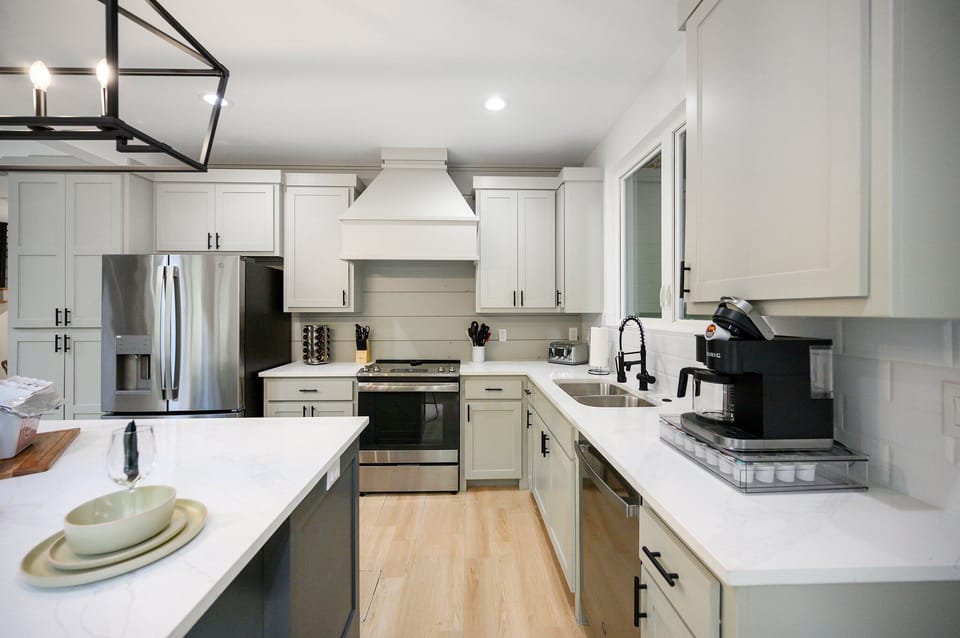 Modern kitchen w/ white cabinets, stainless steel appliances, & coffee maker.