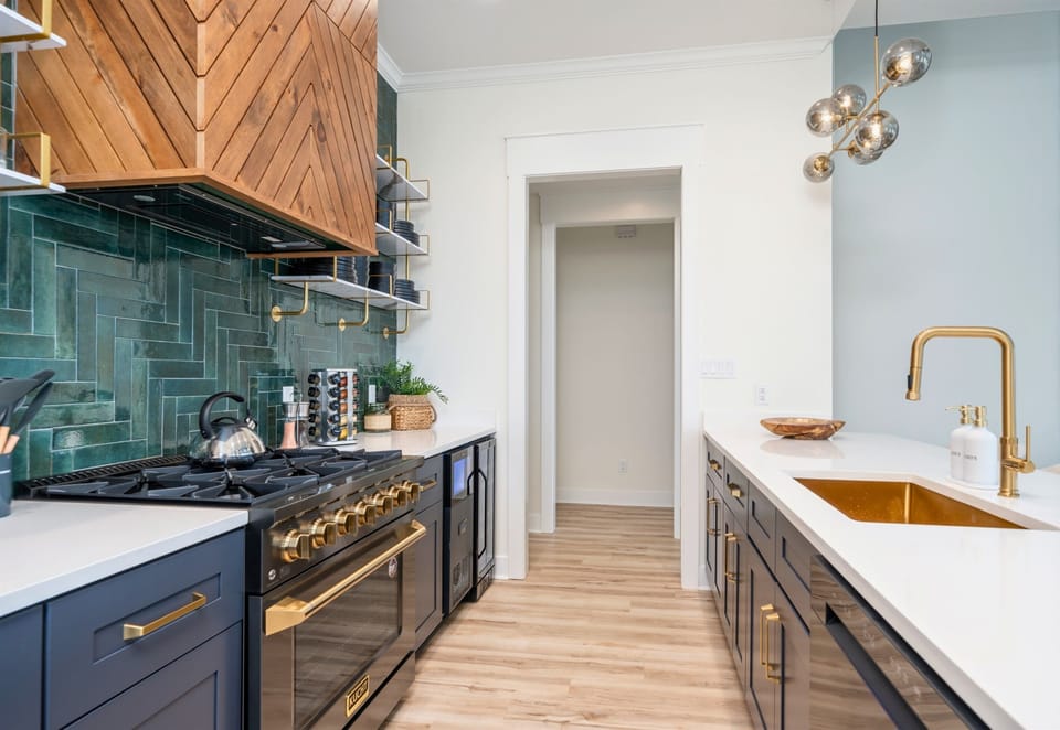 A Modern Kitchen With Sleek Cabinets, Gold Fixtures And A Long Island With White Countertops Extending Into A Casual Dining Area, All Under Warm, Inviting Lighting.