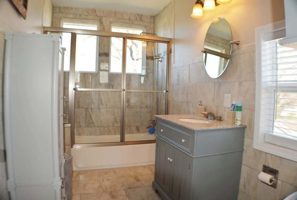 Indulge in luxury in this bathroom oasis. A chic sink and mirror enhance the space, while a bathtub and walk-in shower under a sunlit window create a serene retreat.