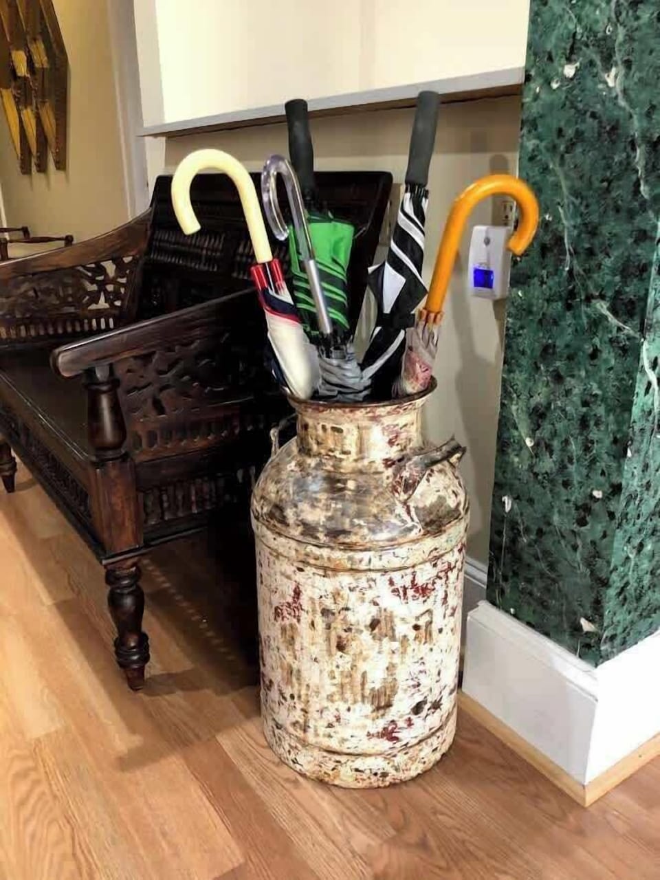 A stylish vase, thoughtfully filled with an assortment of umbrellas, resting gracefully upon the gleaming hardwood floor beside a comfortable chair and an adjacent wall, blending form and function seamlessly.