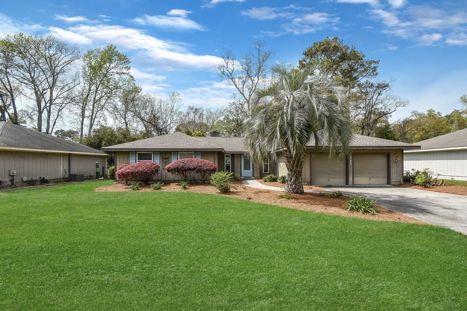 Front Exterior – Welcome to Gone Coastal - A cheerful first impression with a giant palm and manicured lawn—this St. Simons Island beach rental is all charm before you even step inside.